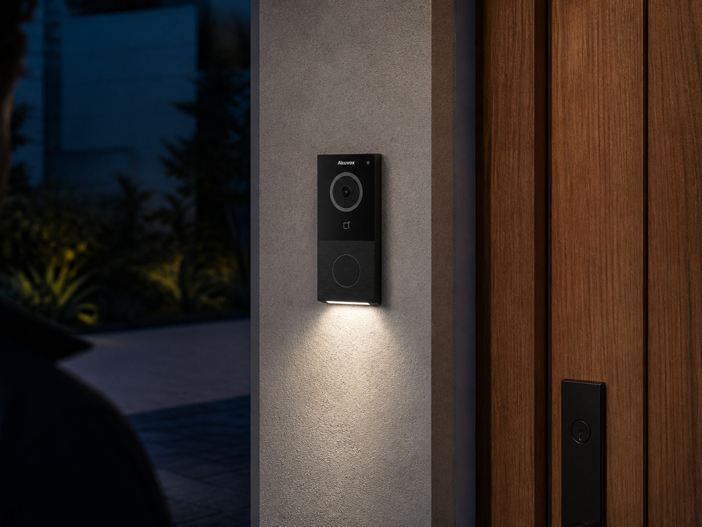 Akuvox E12W black doorbell at dusk with white-light illumination on the approach